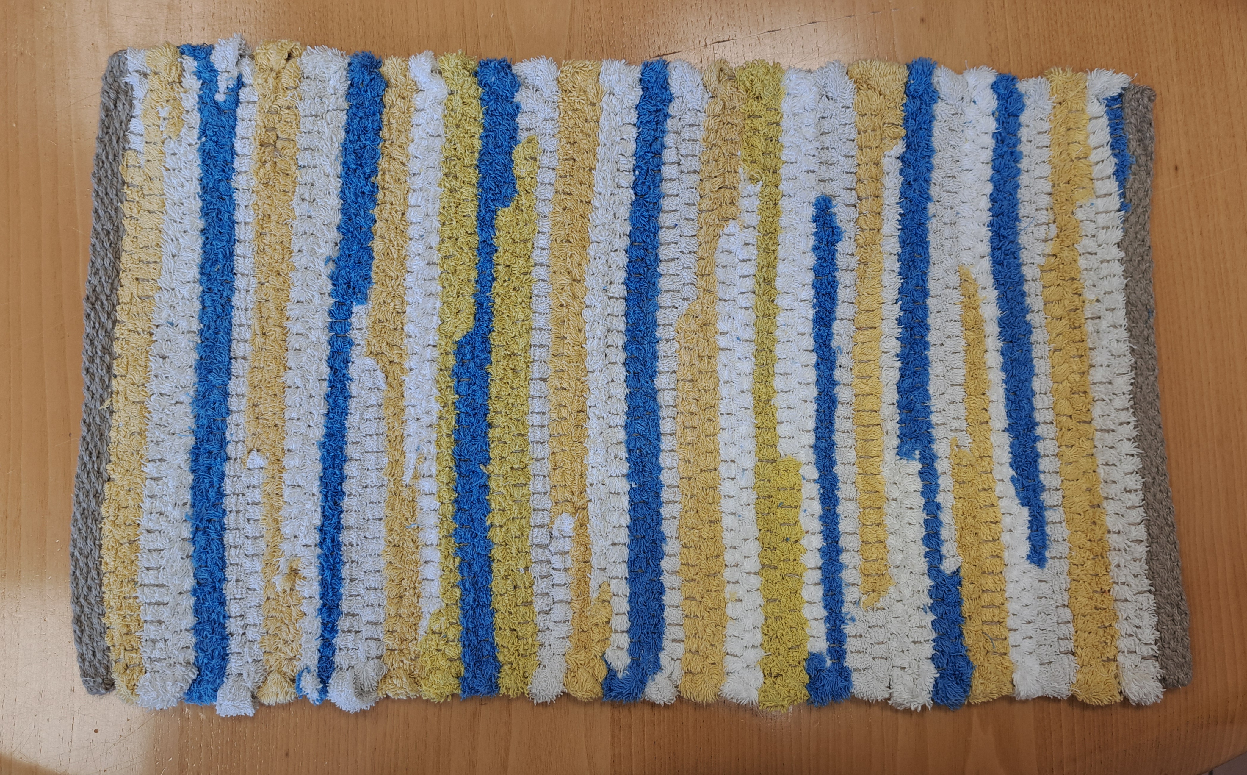 Tappeto artigianale in spugna riciclata, a righe verticali blu, gialle e bianche, realizzato nel laboratorio Handswork