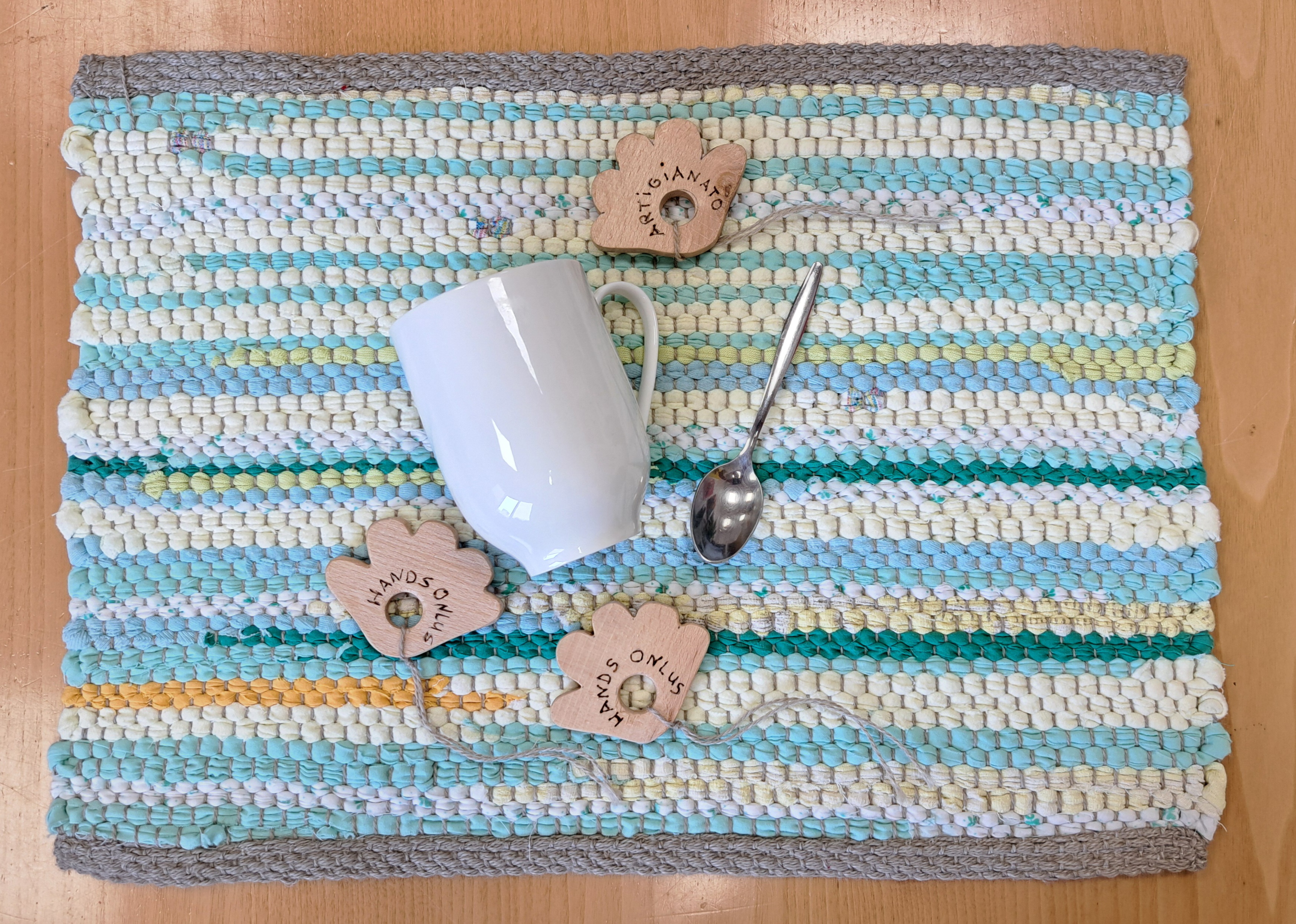 Handgemachtes Tischset aus recyceltem Stoff mit hellblauen und grünen Streifen, dazu eine Tasse, Teelöffel und Etiketten