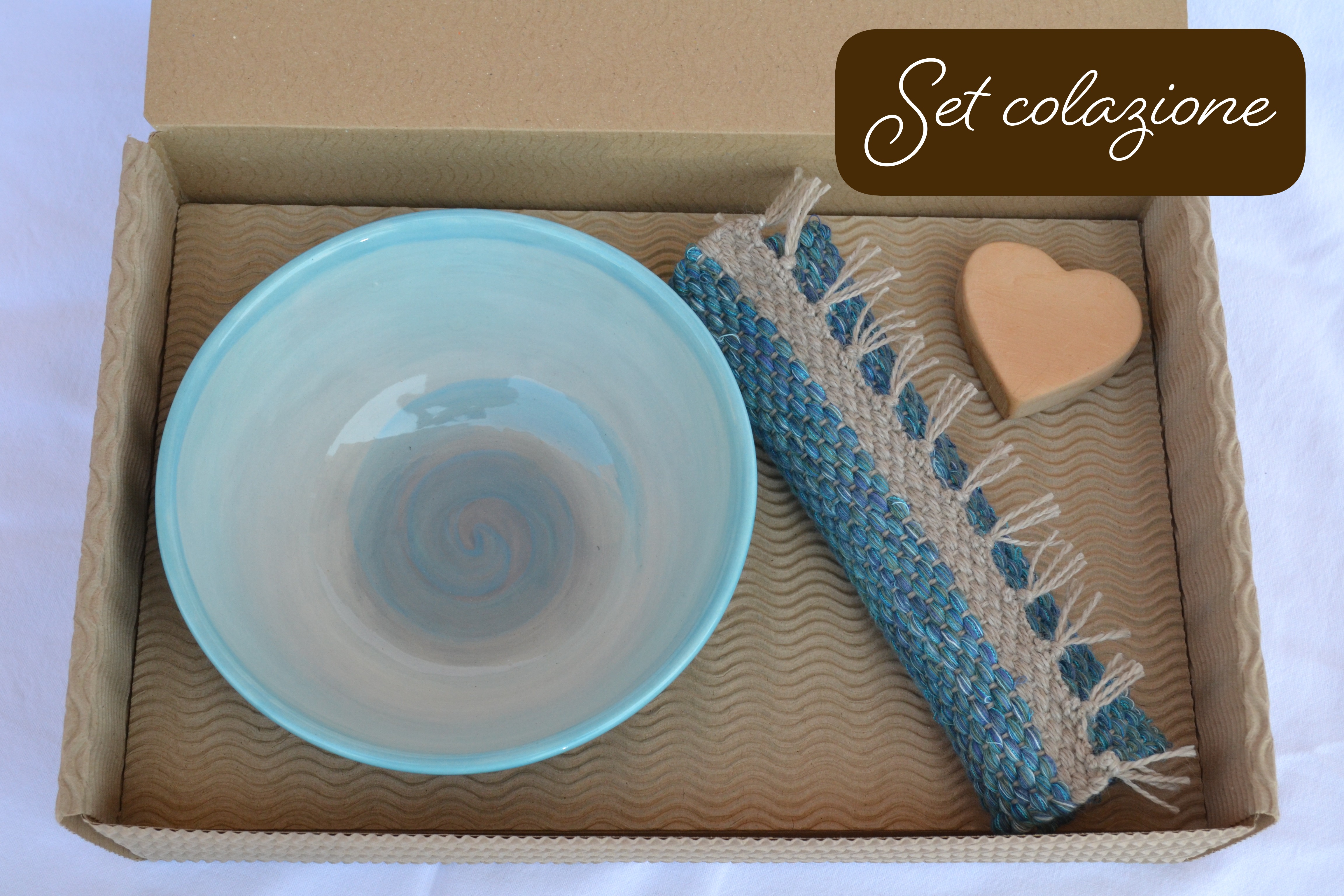 Set colazione artigianale con ciotola in ceramica azzurra, tappeto in tessuto riciclato e sapone a forma di cuore, confezionato in una scatola di cartone ondulato
