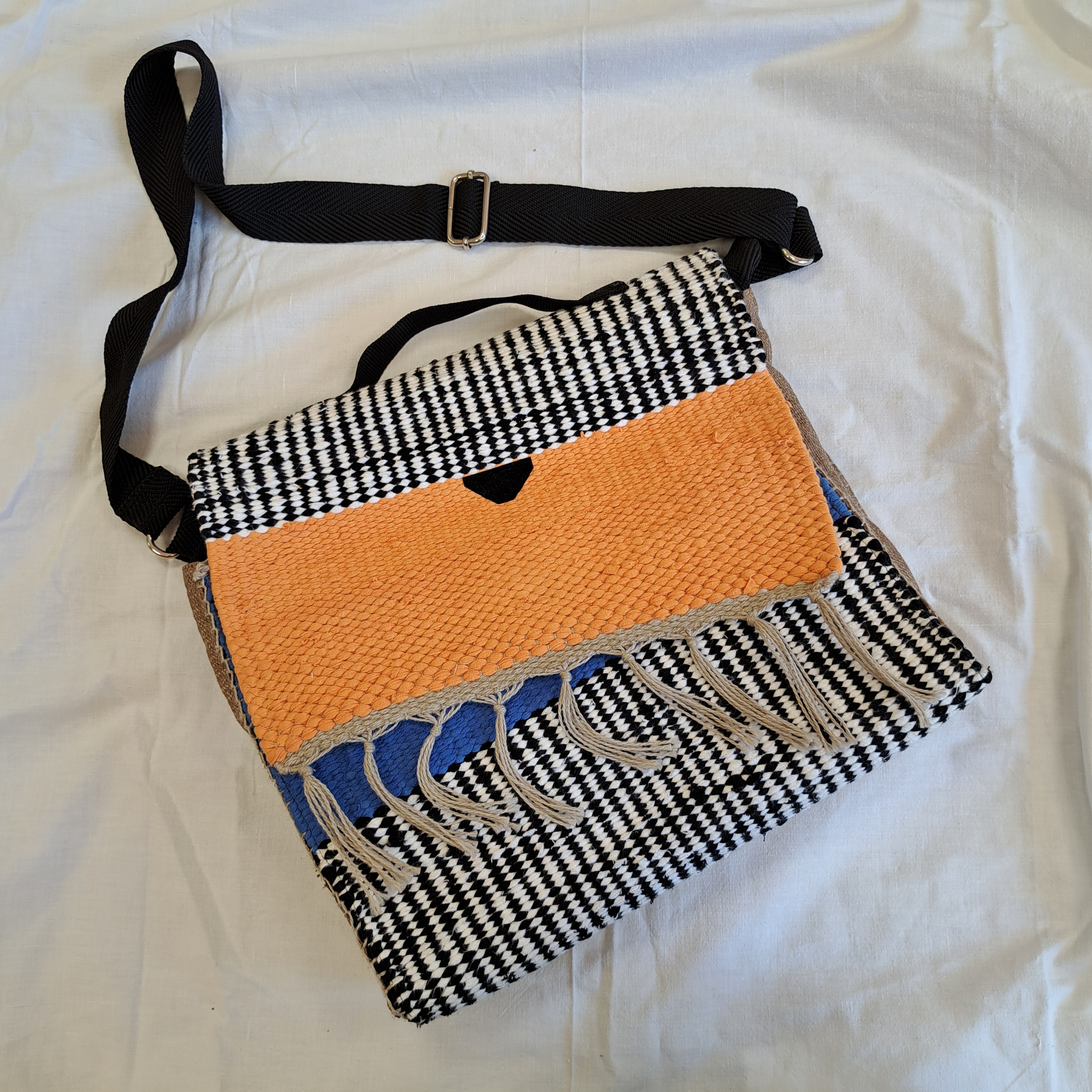 Umhängetasche , mit schwarz-weißem Fischgrätmuster, orangefarbenem Band und Fransen, hergestellt aus recycelten Materialien