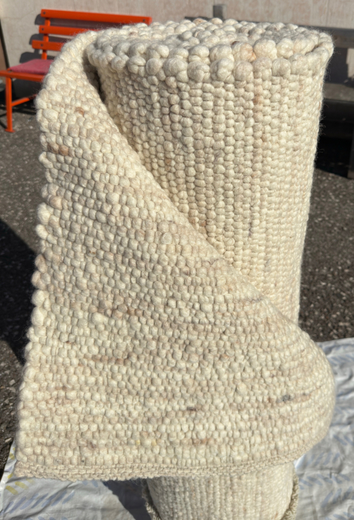 Ein gerollter, handgefertigter Teppich in hellem Beige mit Knotentextur, hergestellt aus recycelten Materialien im HANDS Labor